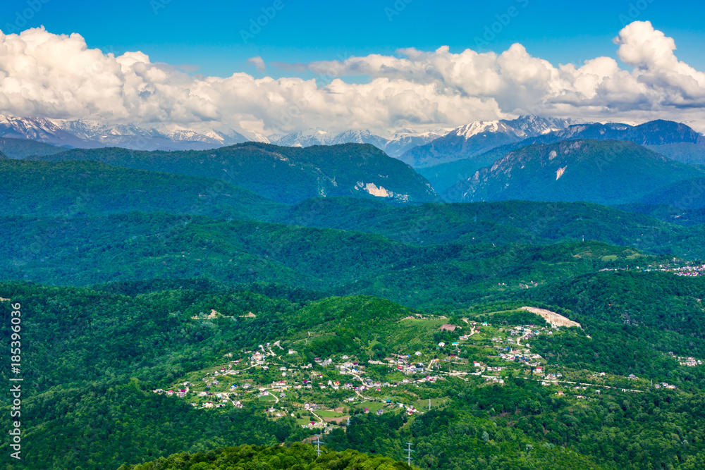 The view of the highland village and Caucasus mountains covered with green forest and snow from the lookout tower on mount Akhun. Khosta district, Adler, Sochi, Russia.