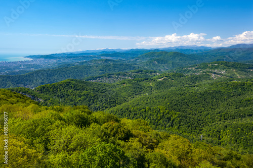 The view of the highland village and Caucasus mountains covered with green forest and snow from the lookout tower on mount Akhun. Khosta district  Adler  Sochi  Russia.