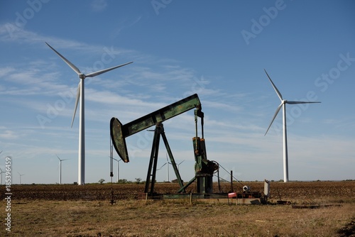Low angle view of a crude oil pump jack framed by wind power turbines, new versus old technology in Texas, USA