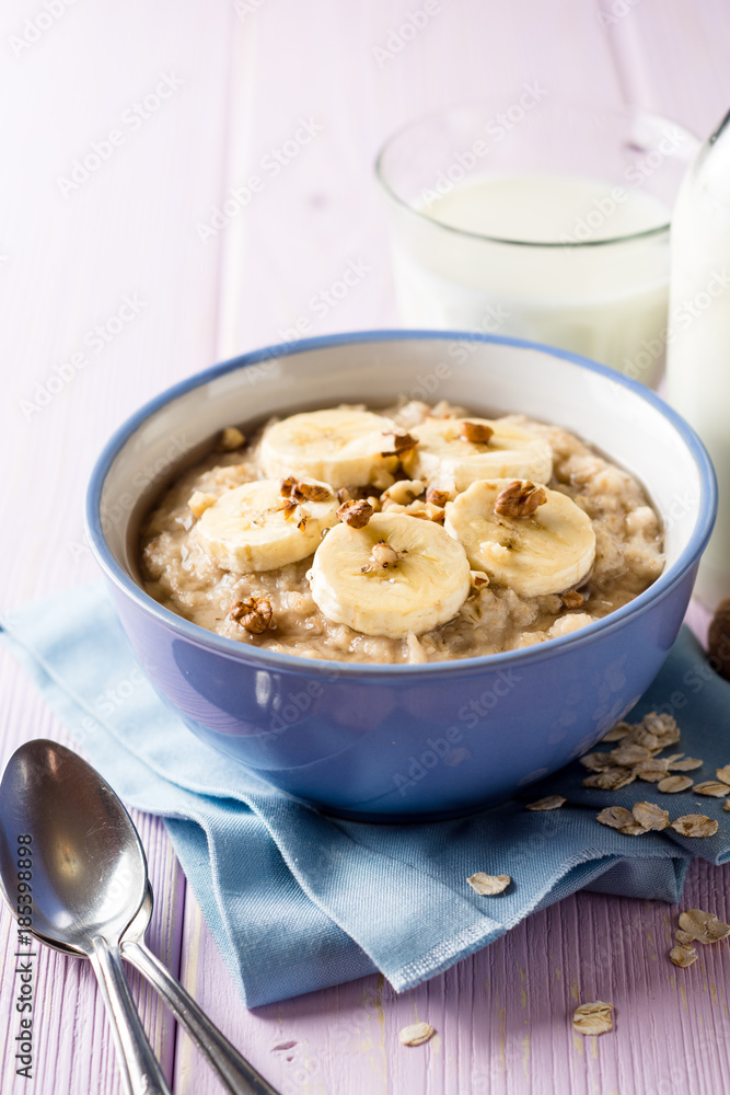 Oatmeal porridge with banana, walnuts and honey in bowl on purple wooden background. Healthy breakfast. Oatmeal porridge with banana, walnuts and honey in bowl on purple wooden background. Healthy breakfast.