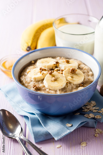 Oatmeal porridge with banana, walnuts and honey in bowl on purple wooden background. Healthy breakfast.