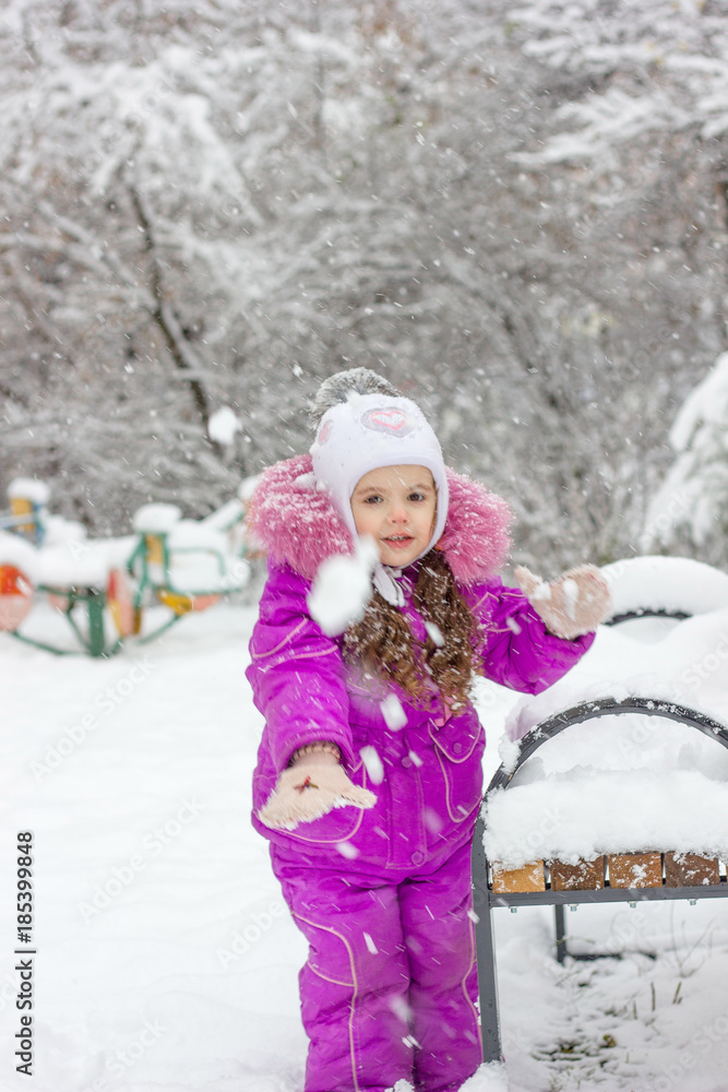 Little girl plays snowballs at winter day outdoors.
