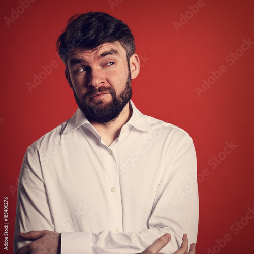 Thinking grimacing bearded fun man in whirt shirt looking on orange background with empty copy space. Closeup toned portrait