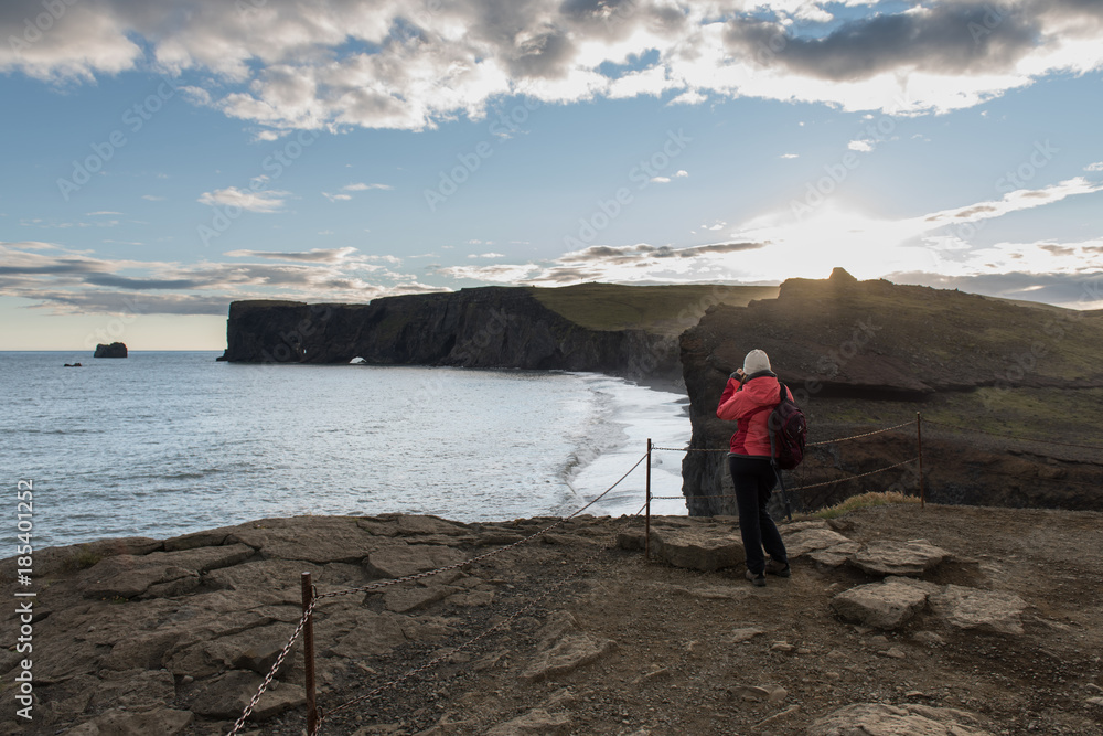 Woman stands on the top of cliff over the black beach
