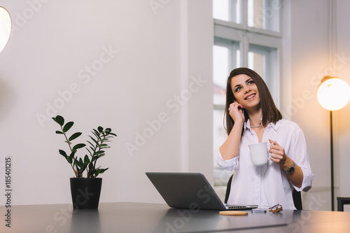 Pretty girl drinking coffee or tea at bright office while listening to the music. © Nebojsa