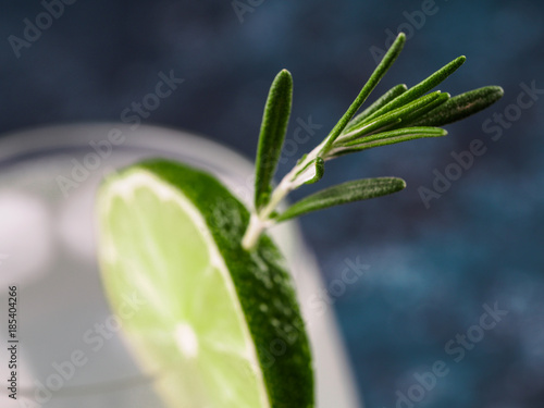 Glass of alcoholic coctail with fresh rosemary and lime on blue background. Close up. Shallow DOF
