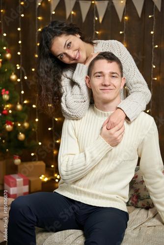 couple in christmas lights and decoration, dressed in white, young girl and man, fir tree on dark wooden background, winter holiday concept