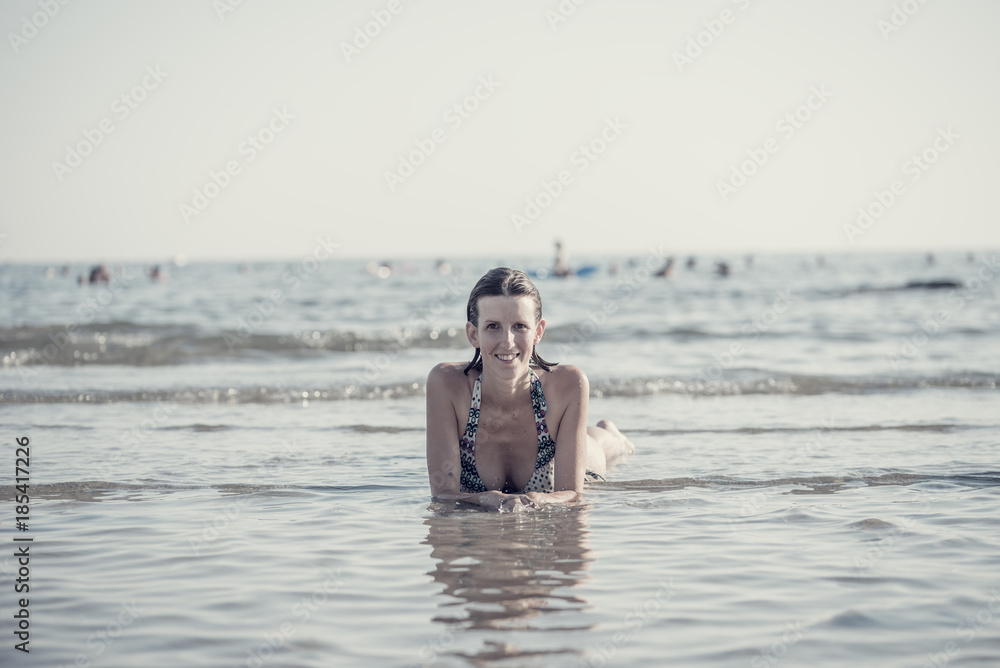 Front view of a smiling woman with wet hair wearing swimsuit lying in sea during summer vacations