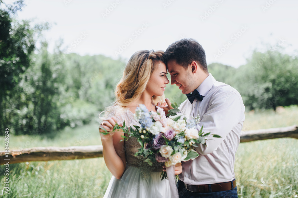 The bride and groom are smiling and looking at each other. The bride is holding a bouquet. Wedding walk in the village. The bride and groom are smiling and looking at each other. The bride is holding a bouquet. Wedding walk in the village.