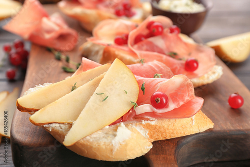 Tasty bruschetta with pear and prosciutto on wooden board, closeup