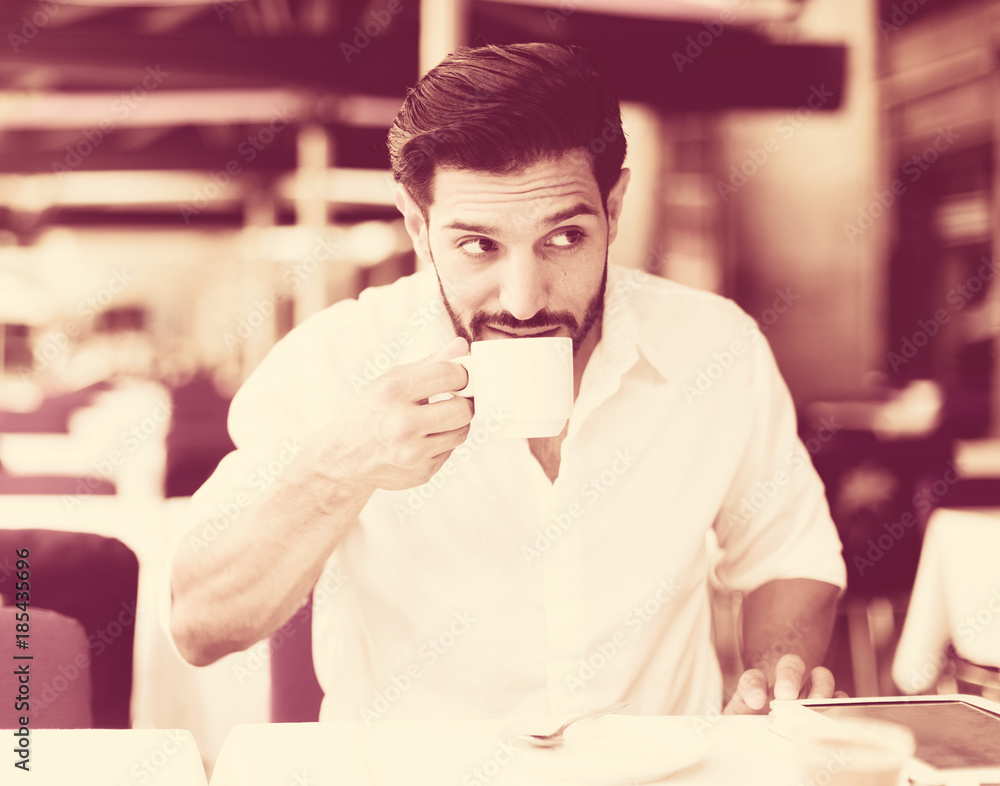 Obraz premium Man drinking coffee in summer cafeteria