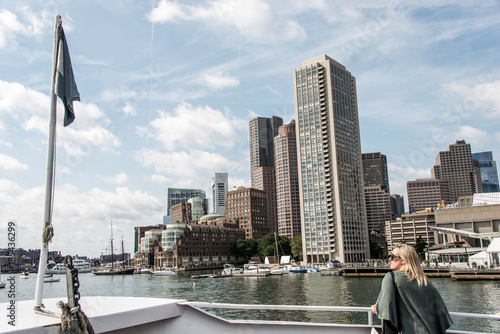 Woman on ferry looking at Sailing boats on Charles River in front of the Boston Skyline on a sunny summer day