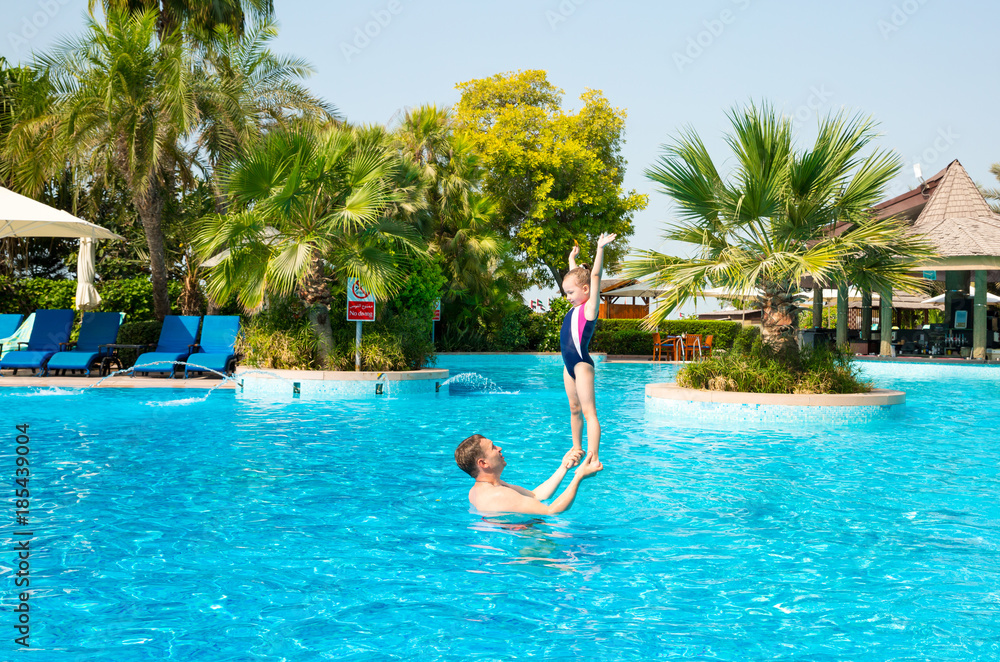 Active father teaching his kid daughter to swim in pool on tropical resort. Summer vacations and sport concept