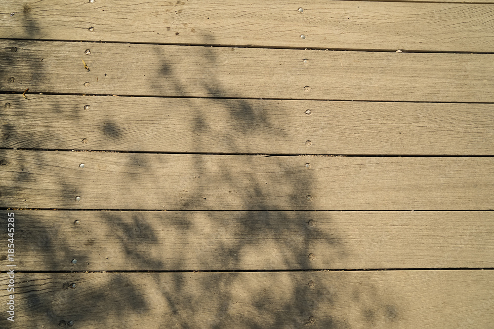 Fototapeta premium Soft abstract natural pattern of olive tree branches shadow on light brown wooden plank strip grain texture surface walkway background on sunny day