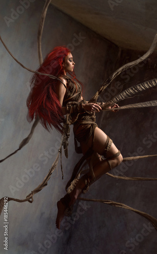 Flying beautiful red haired woman bounding by ropes on dark background