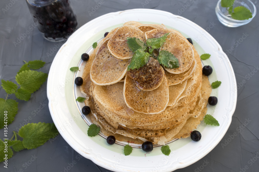 Pancakes are located in a plate on a gray background, decorated with berries and mint leaves. Pancakes are located in a plate on a gray background, decorated with berries and mint leaves.