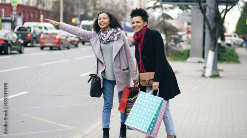 Two attractive african american women with shopping bags calling for taxi cab while coming back from mall sales