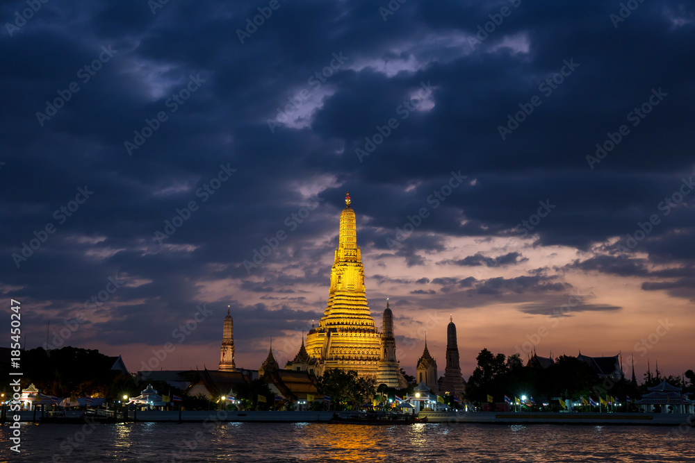 Landscape image of temple of dawn or Wat Arun and Chao Phraya River in the front when the sunset at dusk time is beautiful with warm gold color tone.