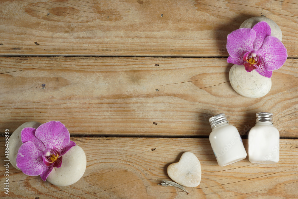 Body lotion and stones for a hot massage are spread out on a wooden table before the spa procedure. Ornament of beautiful orchid flowers. Body lotion and stones for a hot massage are spread out on a wooden table before the spa procedure. Ornament of beautiful orchid flowers.