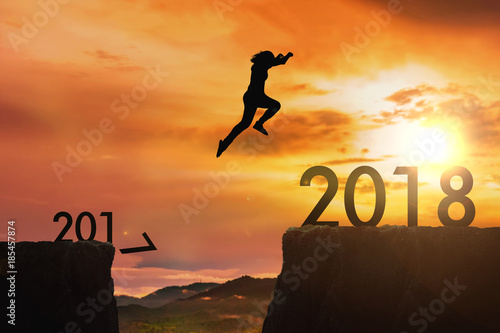 Siluate woman jumping from 2017 cliff to 2018 cliff on sunrise time : meaning to going to year 2018 photo