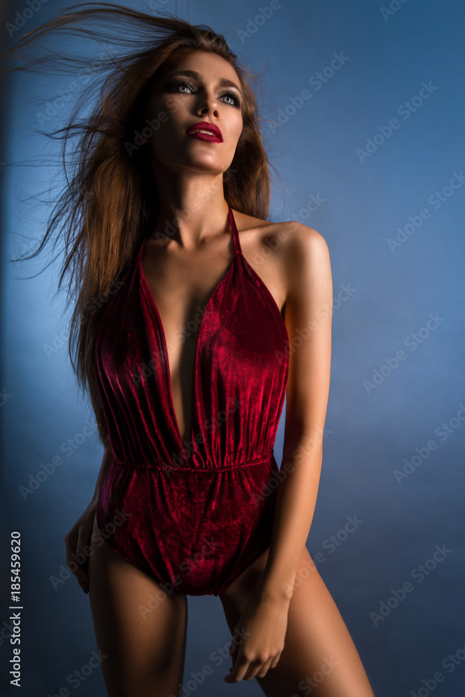 Pretty woman in red bodysuit posing at camera against blue background Pretty woman in red bodysuit posing at camera against blue background