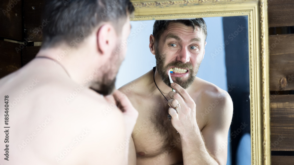 Fototapeta premium bearded man brushing his teeth in front of mirror in bathroom