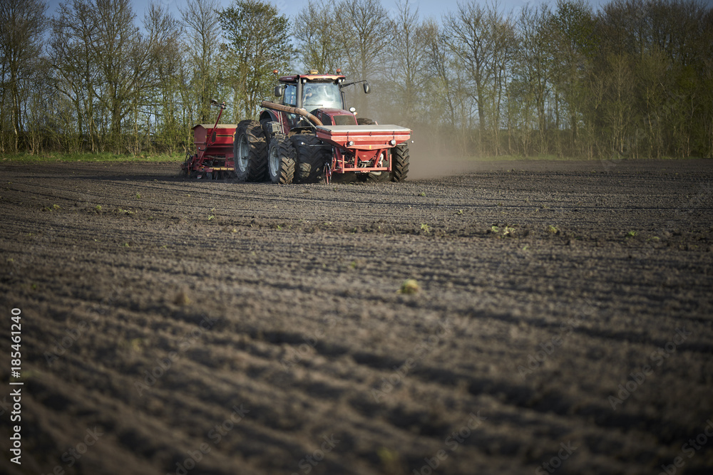 Fototapeta premium Red tractor with sowing machine on a ploughed field