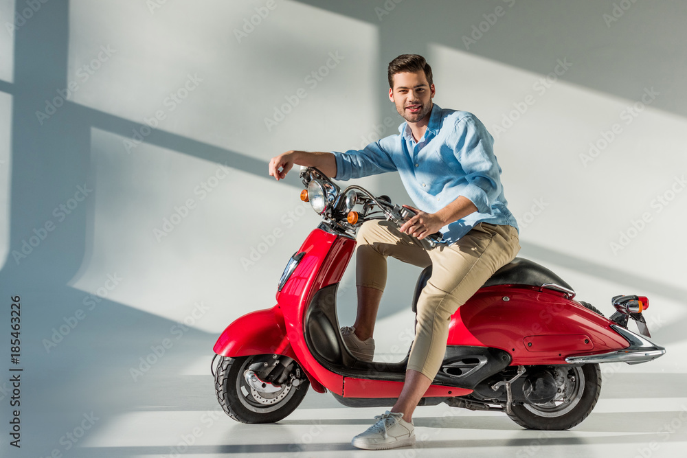 side view of young man looking at camera while sitting on red scooter