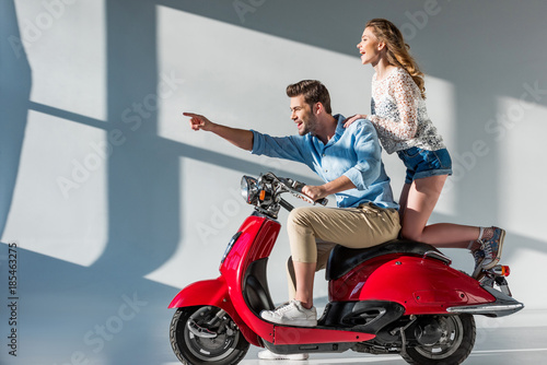 side view of smiling man pointing away while sitting on scooter together with girlfriend
