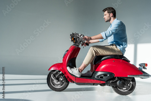 side view of fashionable young man riding red scooter