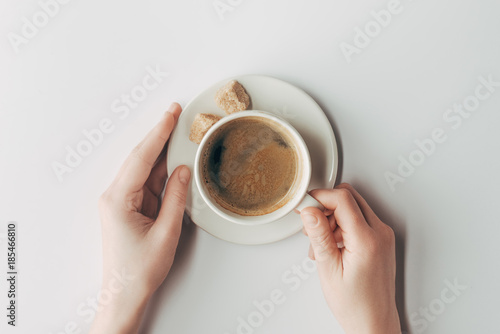 top view of human hands and cup of coffee with sugar on white