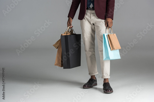 low section of man with paper shopping bags on grey background