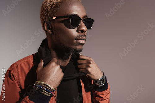 Obraz na płótnie Stylish young african american man straightens his jacket isolated on light background