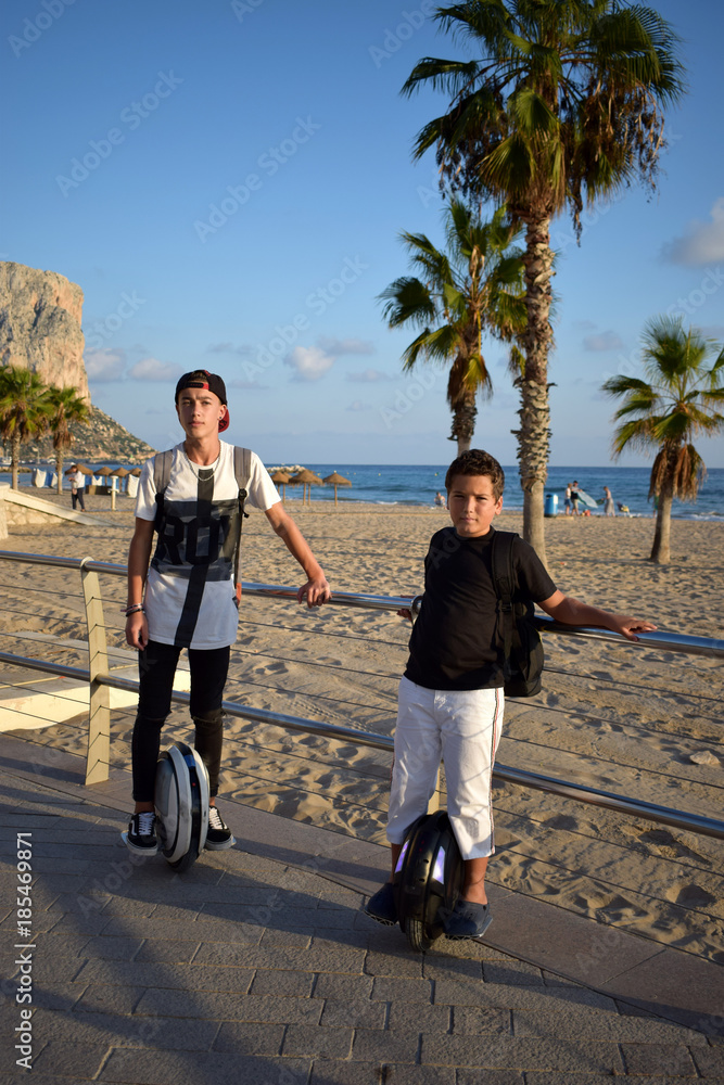 Obraz premium Young boys are riding MonoWheels, Elecrtic Scooters enjoying the ride on a beach promenade