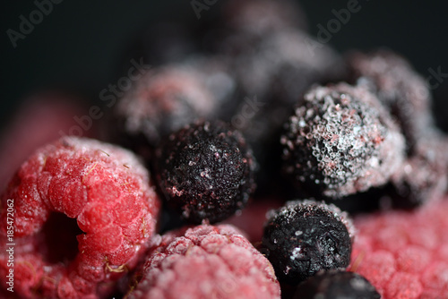 Frozen raspberries and blueberries on a dark background close up