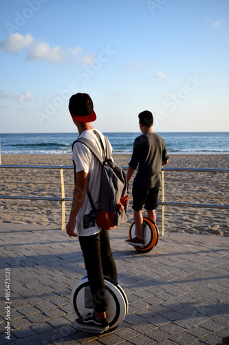 Boys are enjoying riding Monowheels scooters on a beach promenade photo