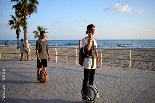 Boys are enjoying riding Monowheels scooters talking on the mobile phone on a beach promenade photo