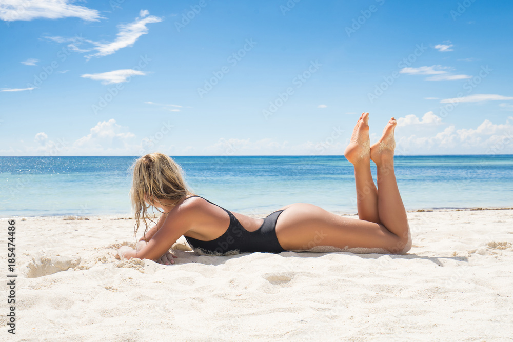 Woman in black swimwear tanning on the beach.