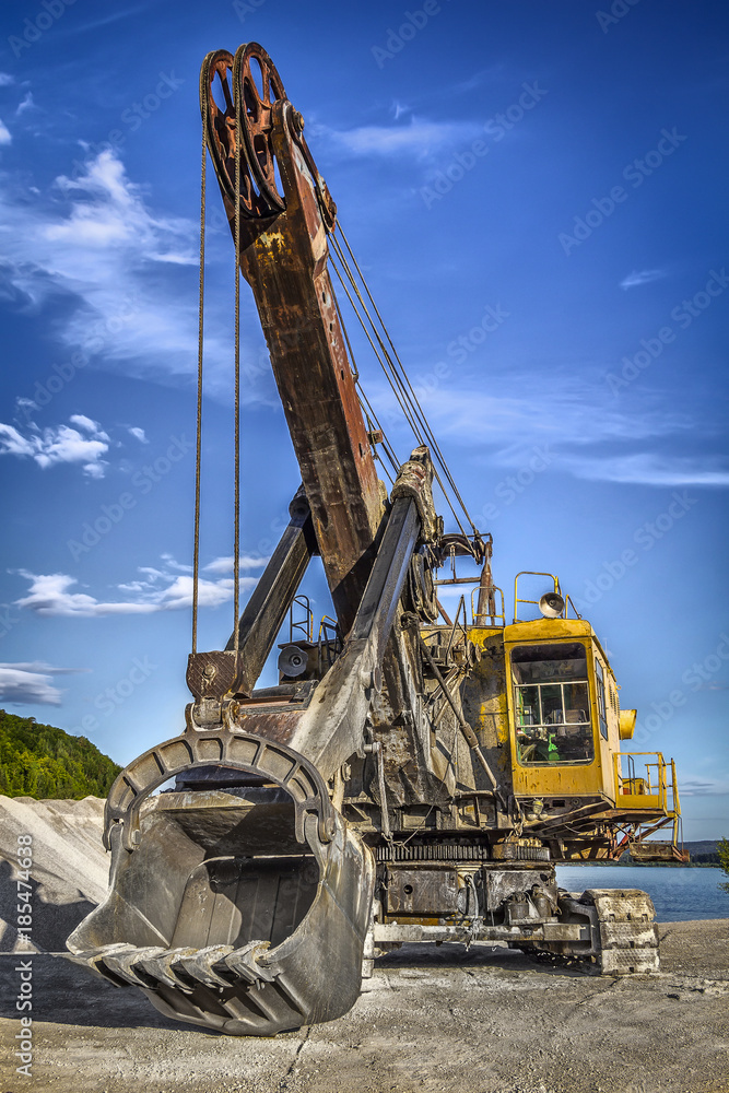 Old yellow excavator on the background of blue sky.