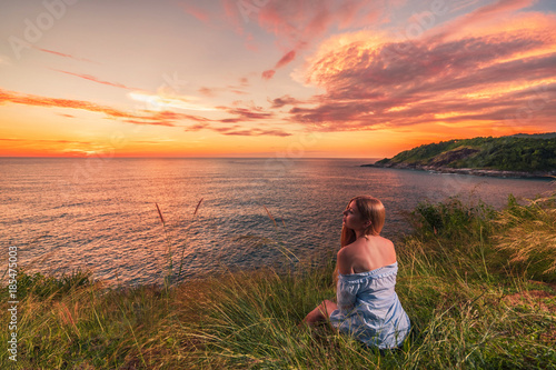 Woman enjoying beautiful colorful sunset above sea from cape. © upslim