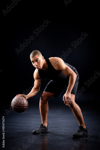 african american basketball player bouncing ball on black