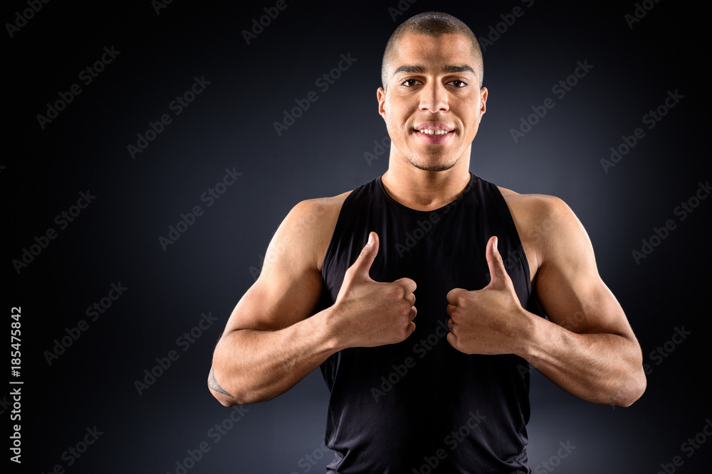 happy african american sportsman showing thumbs up on black