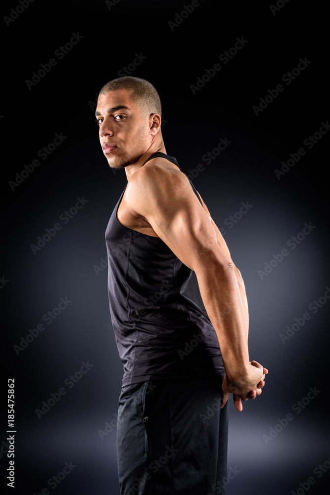 african american sportsman stretching shoulders before workout on black