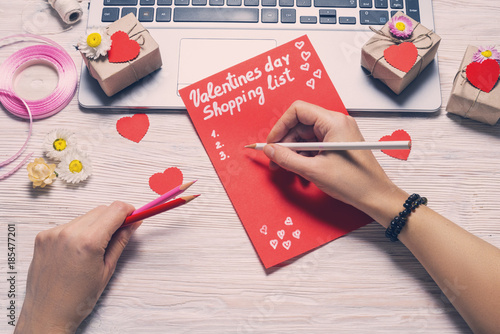 Hands wrinning down Valentines day shopping list on wooden desk photo