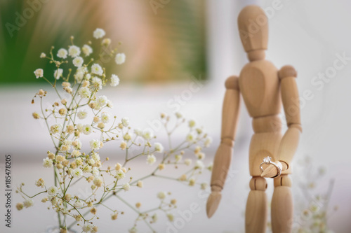 Wooden small mannequin with engagement ring on blurred background