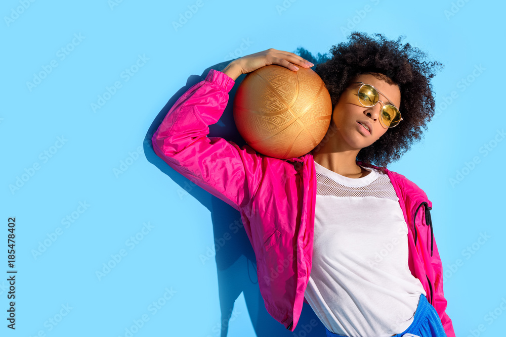  Young girl in glasses holding basketball ball and looking at camera  on blue background