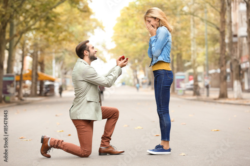Young man with engagement ring making proposal to his beloved girlfriend outdoors
