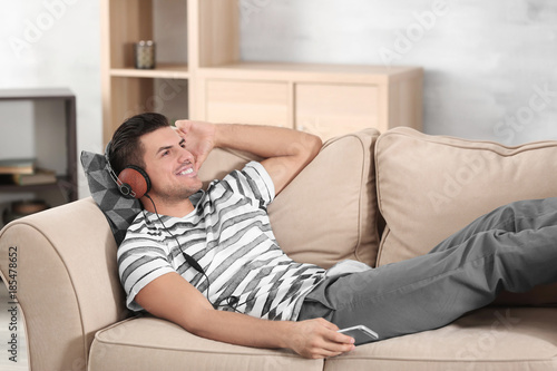 Handsome man listening to music while resting on sofa at home
