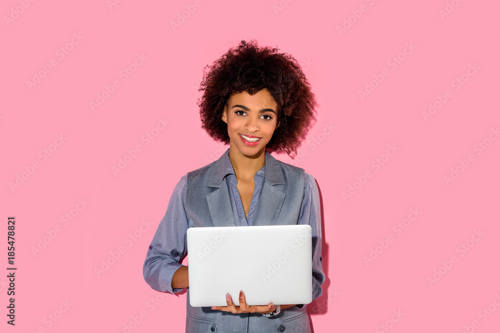 Young african amercian smiling businesswoman holding laptop on pink background Young african amercian smiling businesswoman holding laptop on pink background