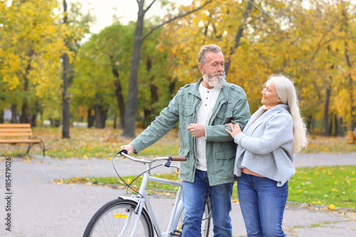 Senior couple walking with bicycle in park